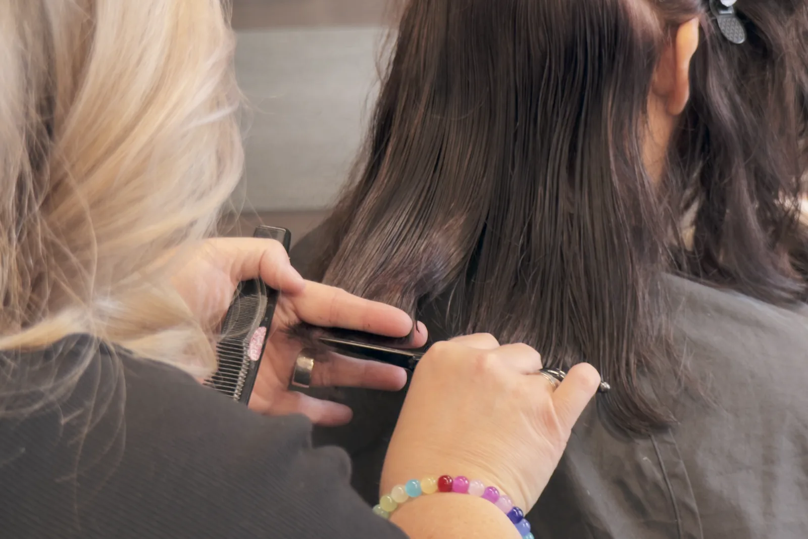 Friseurin schneidet dunkles Haar mit Kamm und Schere
